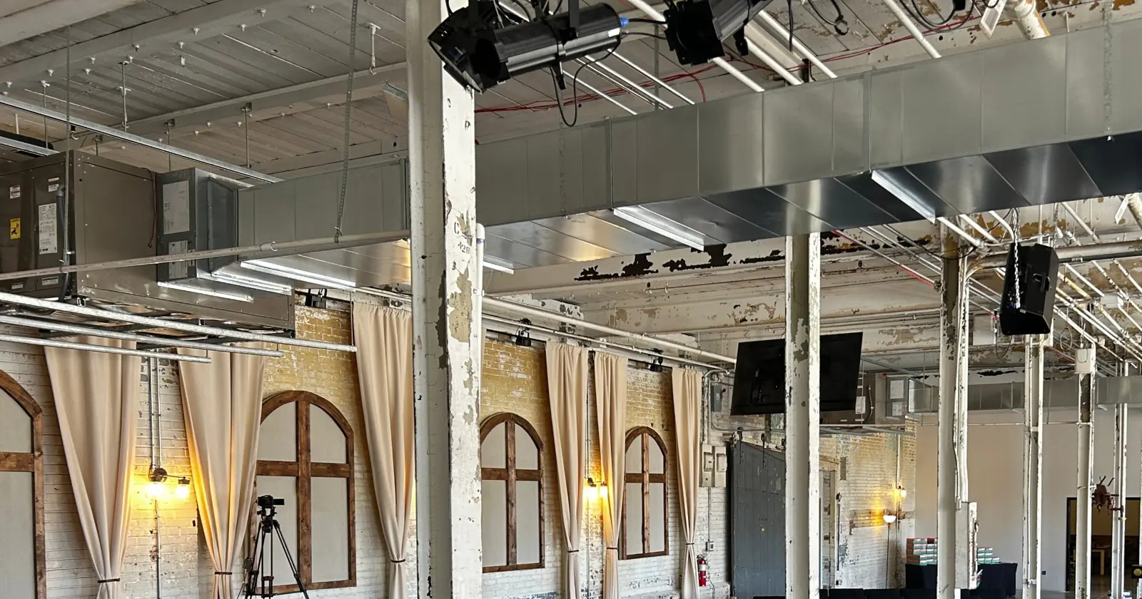 Arched window frames, gold curtains and warm sconces along the brick wall of The Loom